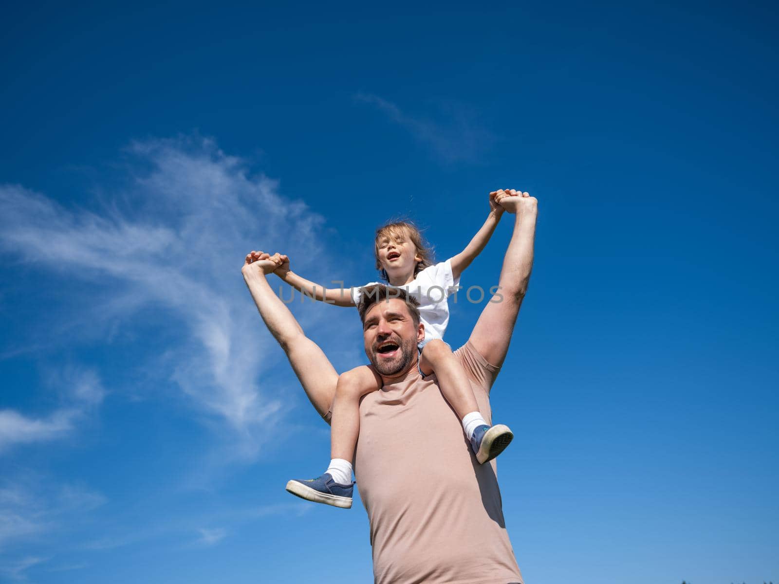 Portrait of happy man holding his little daughter on neck while having rest on summer day