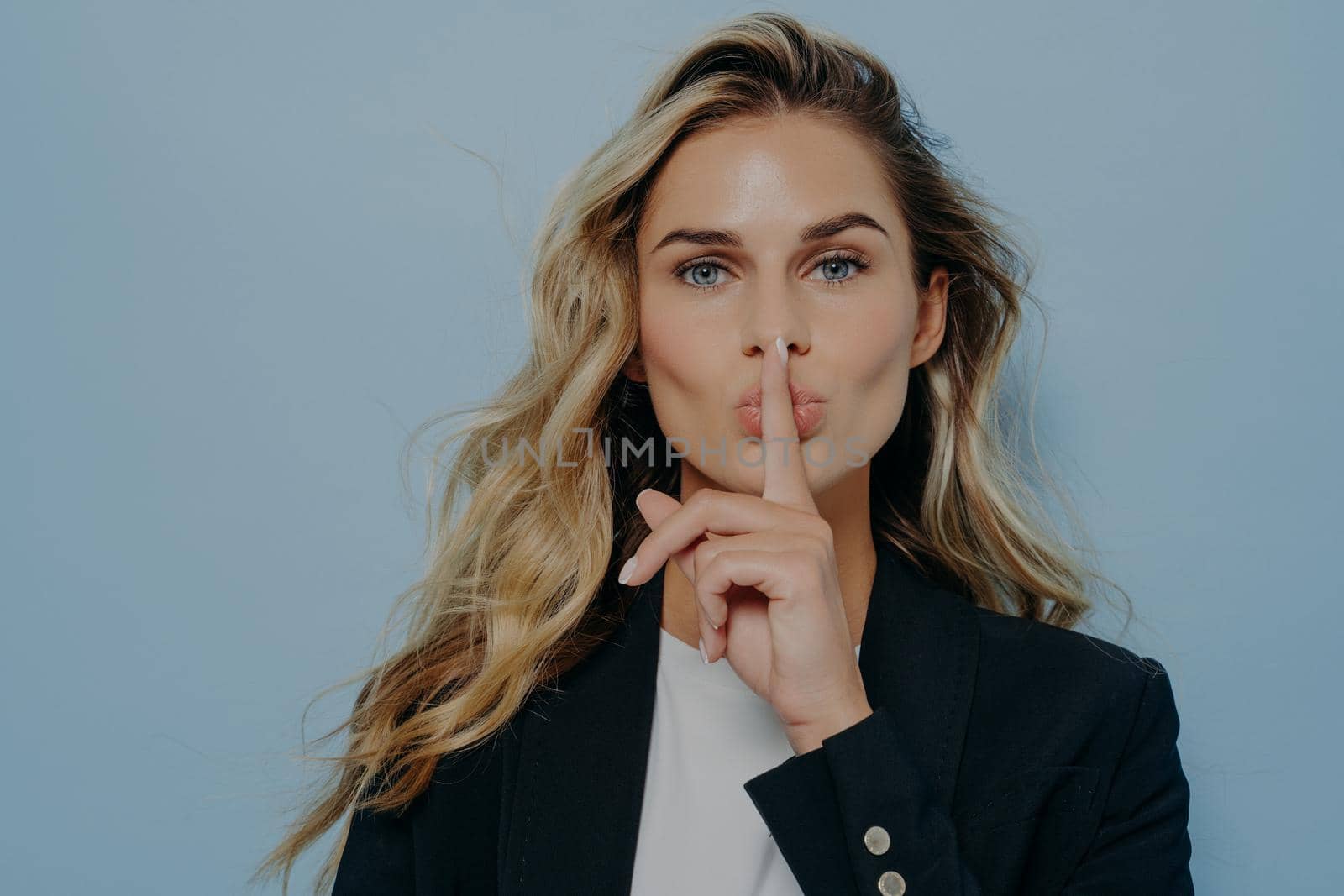 Blonde woman making shush gesture with her hand by vkstock
