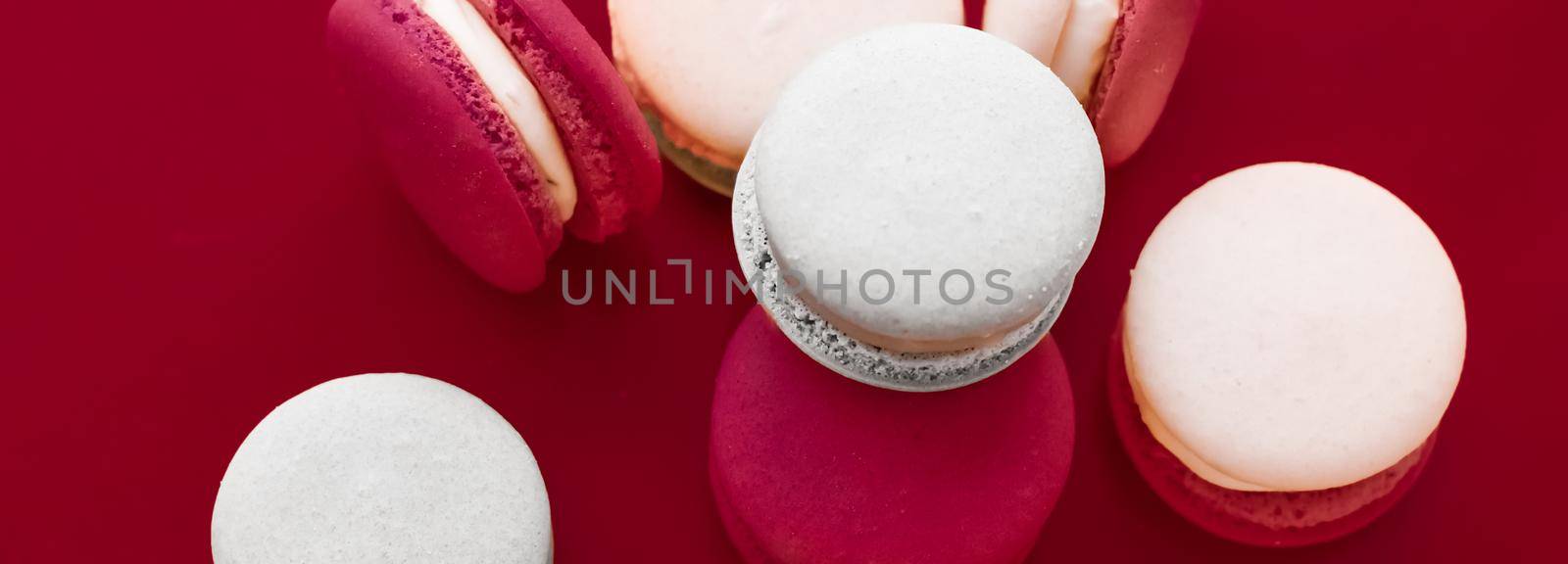 French macaroons on wine red background, parisian chic cafe dessert, sweet food and cake macaron for luxury confectionery brand, holiday backdrop design by Anneleven