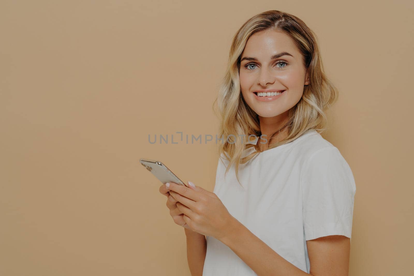Portrait of cheerful young woman in white tshirt being happy to read good news on smartphone by vkstock