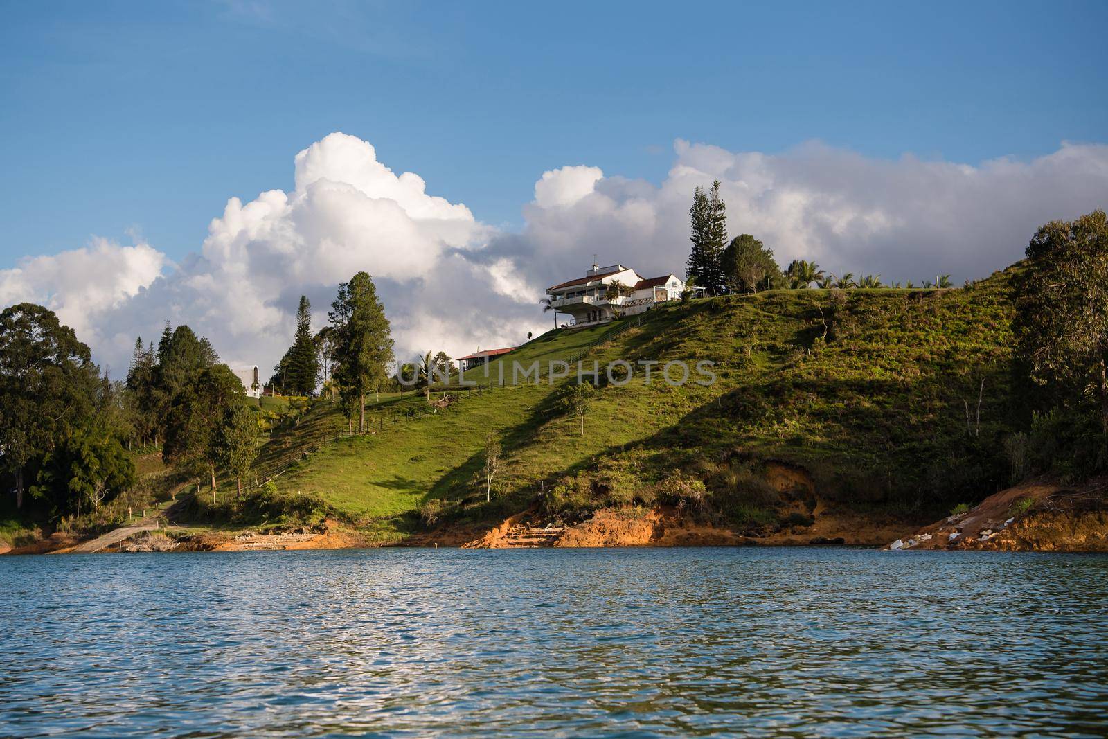 Grassy hillside with cloudy blue sky in the background and water in the foreground. View from a boat