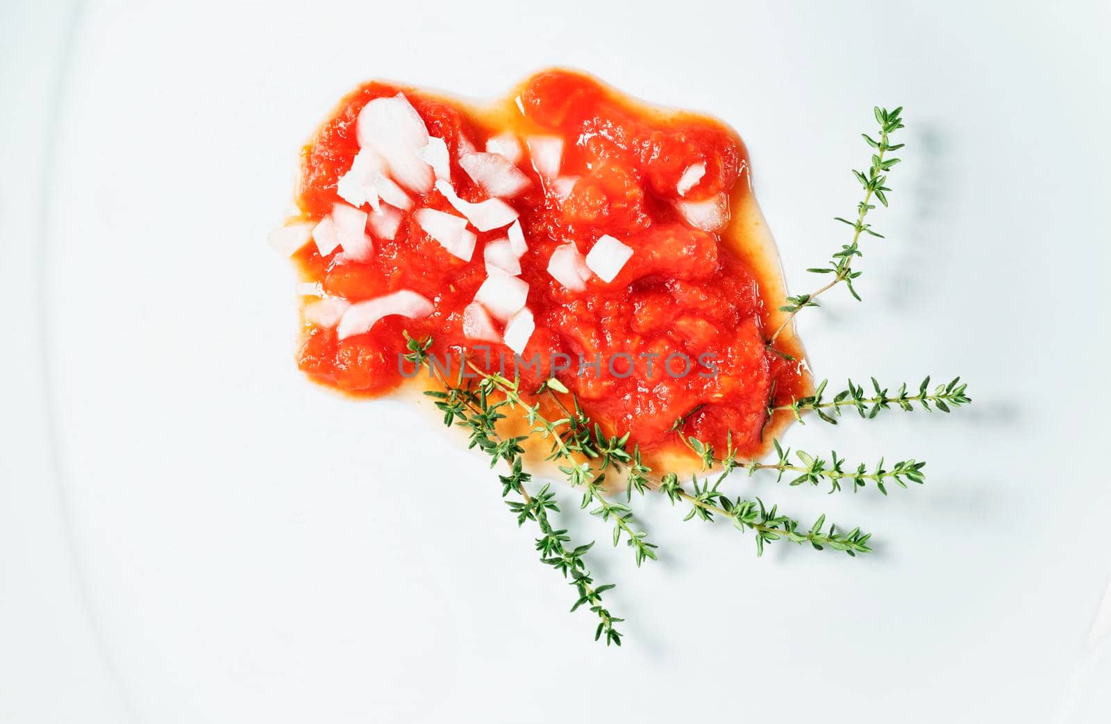Fresh tomato sauce with pieces of white onion and thyme twigs on white plate , preparing food