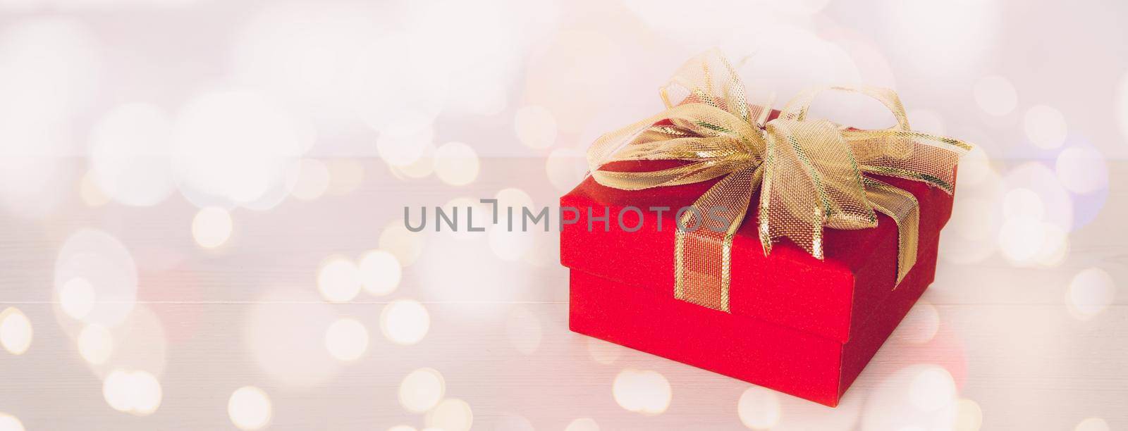 Red gift box on wooden table with bokeh background, love and romance, presents in celebration and anniversary with surprise on desk, happy birthday, copy space, nobody, valentine day concept.