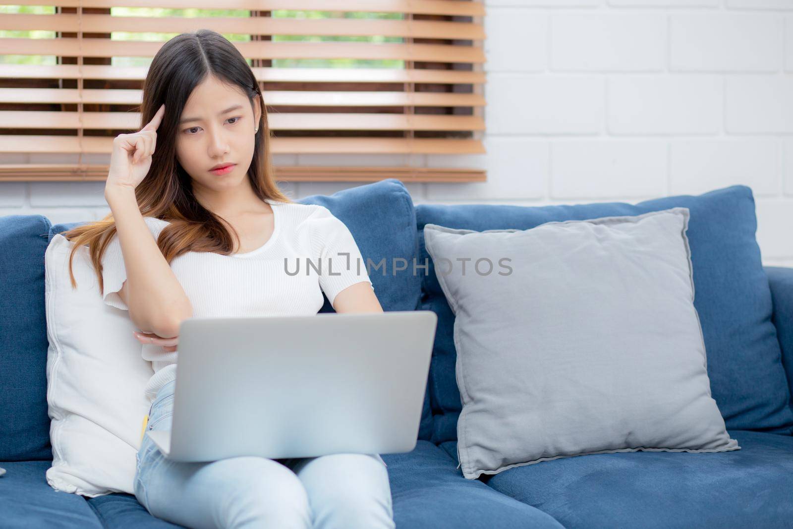 Young asian woman work on laptop computer on sofa at home with frustrated and bored, freelance girl unhappy and tired with unsuccessful, upset from problem, failure and mistake, business concept. by nnudoo