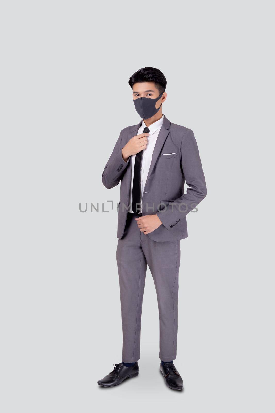 Portrait young asian businessman in suit wearing face mask for protective covid-19 isolated on white background, business man hand holding neck tie, quarantine for pandemic coronavirus, new normal. by nnudoo