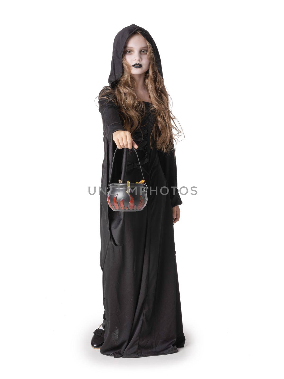 Portrait of little girl in black cloak clothing with cauldron basket of worm sweets isolated on white background, Halloween witch costume, party time, going trick or treating.