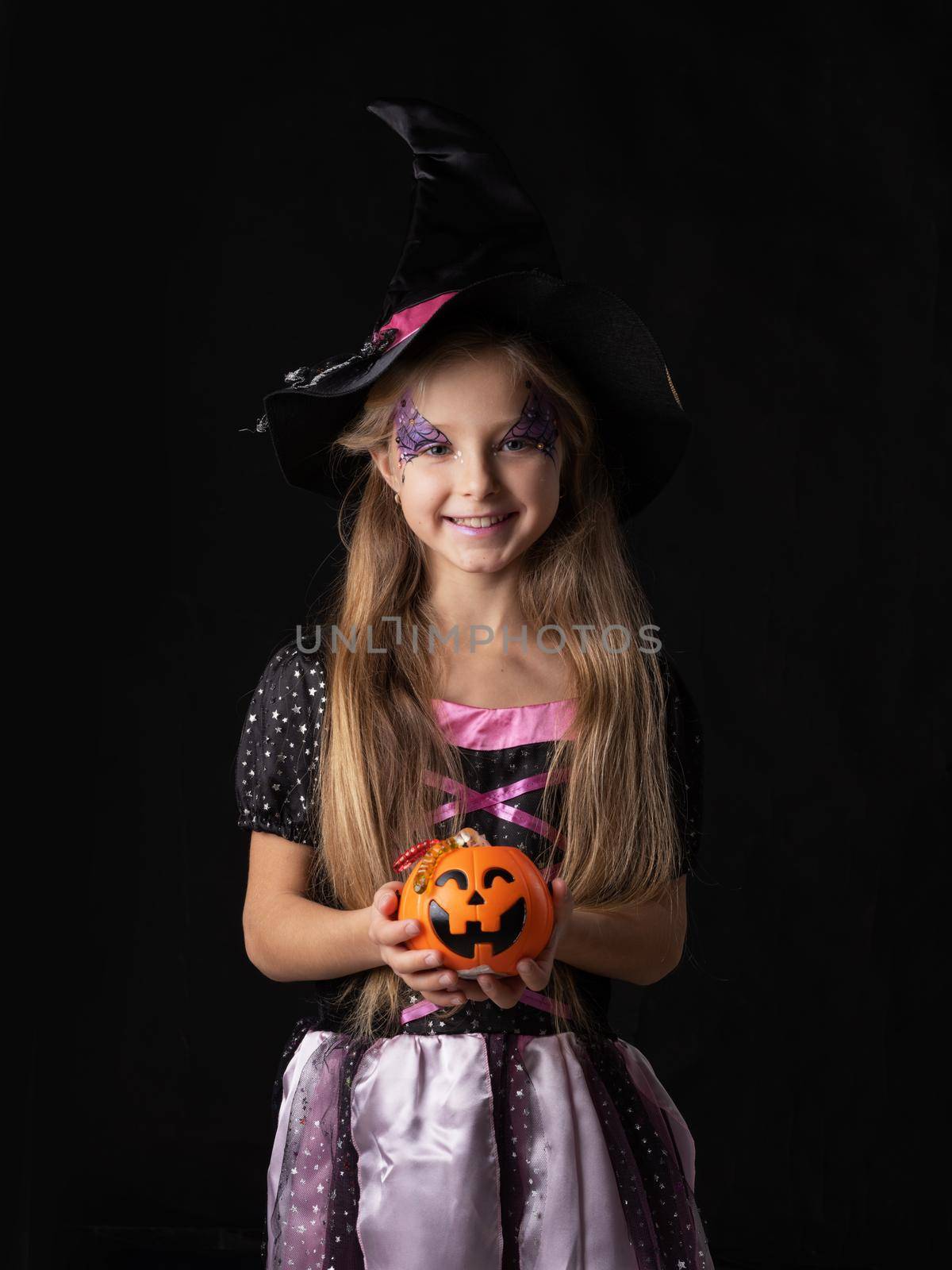 Cute halloween witch girl in fantasy costume holding pumpkin bucket with candy worms, isolated on black background