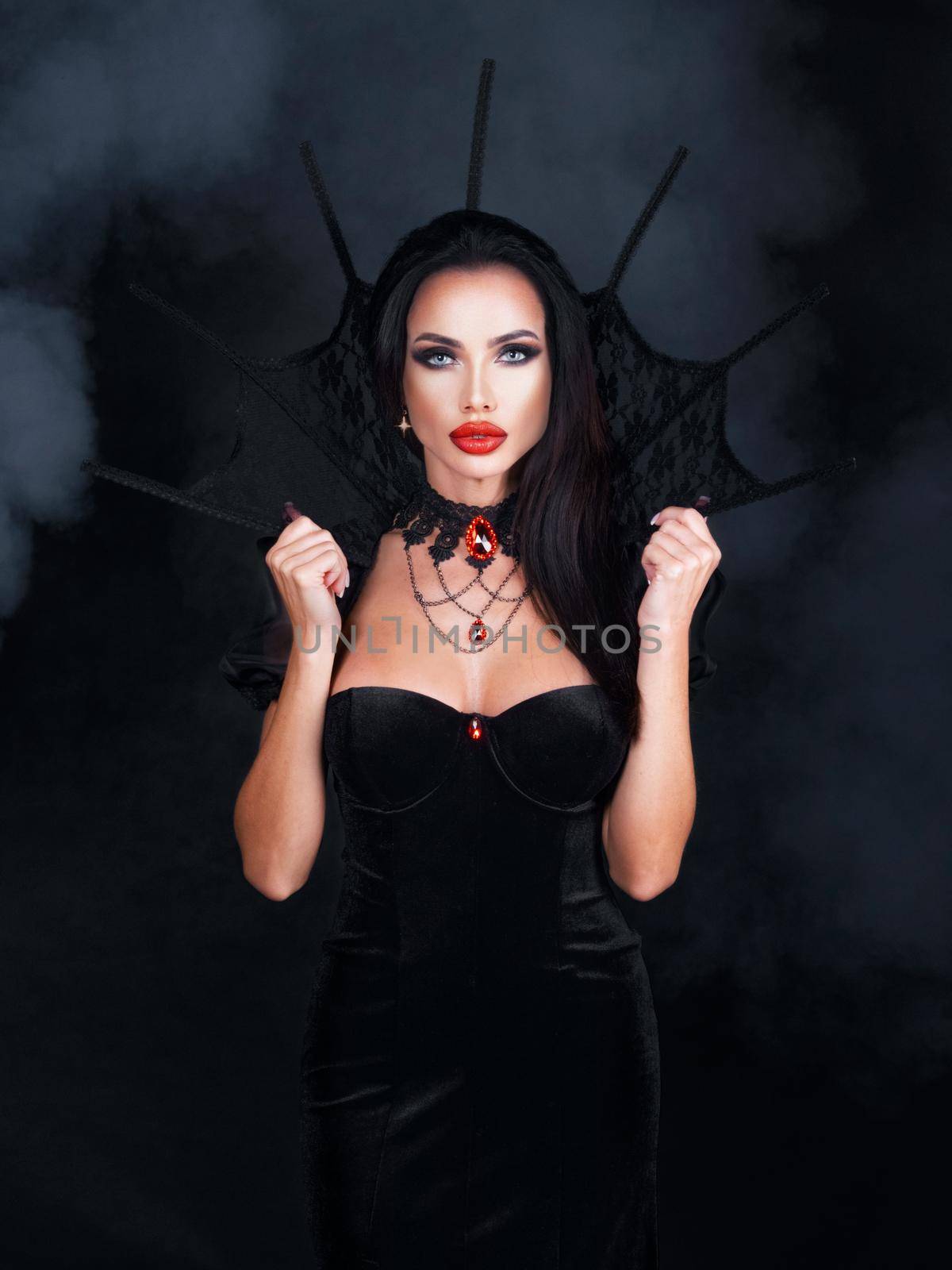Beautiful young woman as sexy vampire in black dress with high collar and red gemstone jewelry - halloween portrait
