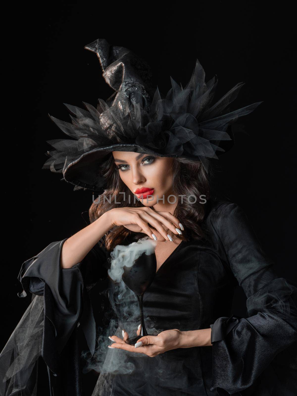 Beautiful sorceress woman in Halloween witch costume dress put a spell smoke in hands isolated on black background
