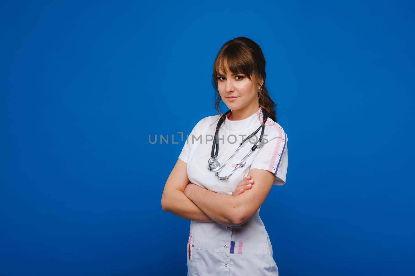 A female doctor, gesticulating, checks the heartbeat in the doctor's office at the hospital with a stethoscope isolated on a blue background by Lobachad