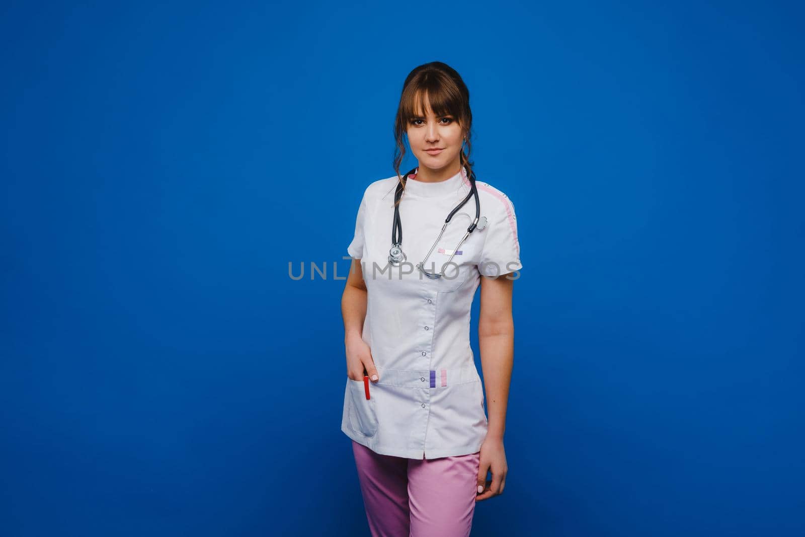 A female doctor, gesticulating, checks the heartbeat in the doctor's office at the hospital with a stethoscope isolated on a blue background by Lobachad