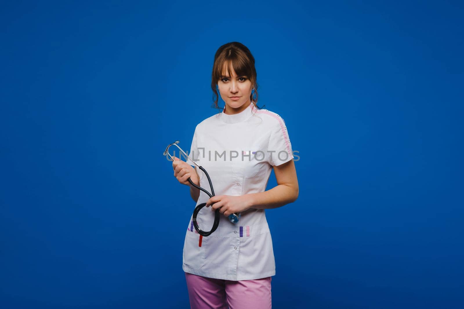 A female doctor, gesticulating, checks the heartbeat in the doctor's office at the hospital with a stethoscope isolated on a blue background.