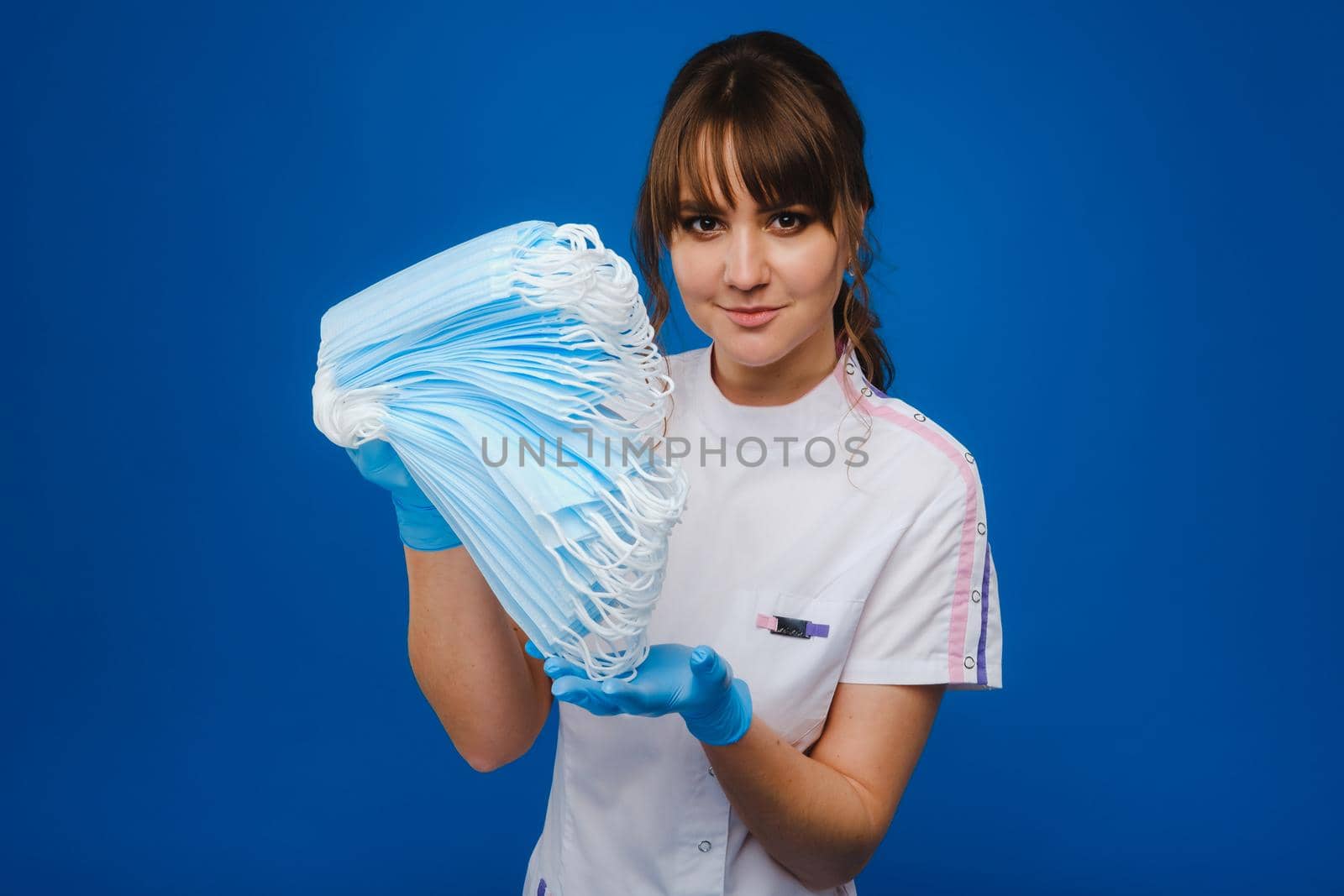 the doctor is holding a bunch of medical masks stacked together on a blue isolated background.