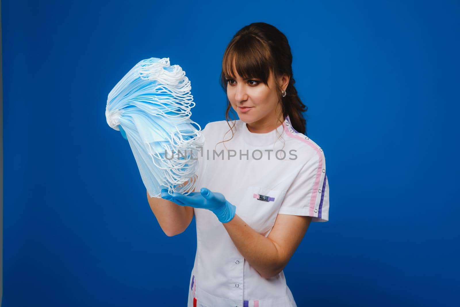 the doctor is holding a bunch of medical masks stacked together on a blue isolated background by Lobachad