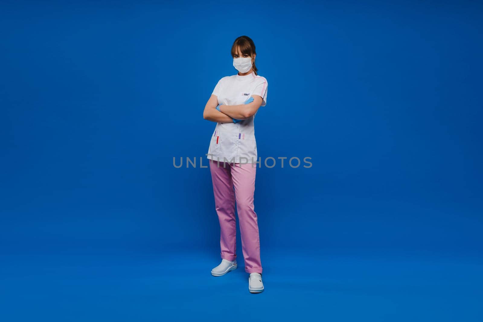 A girl doctor stands in a medical mask and gloves on an isolated blue background.