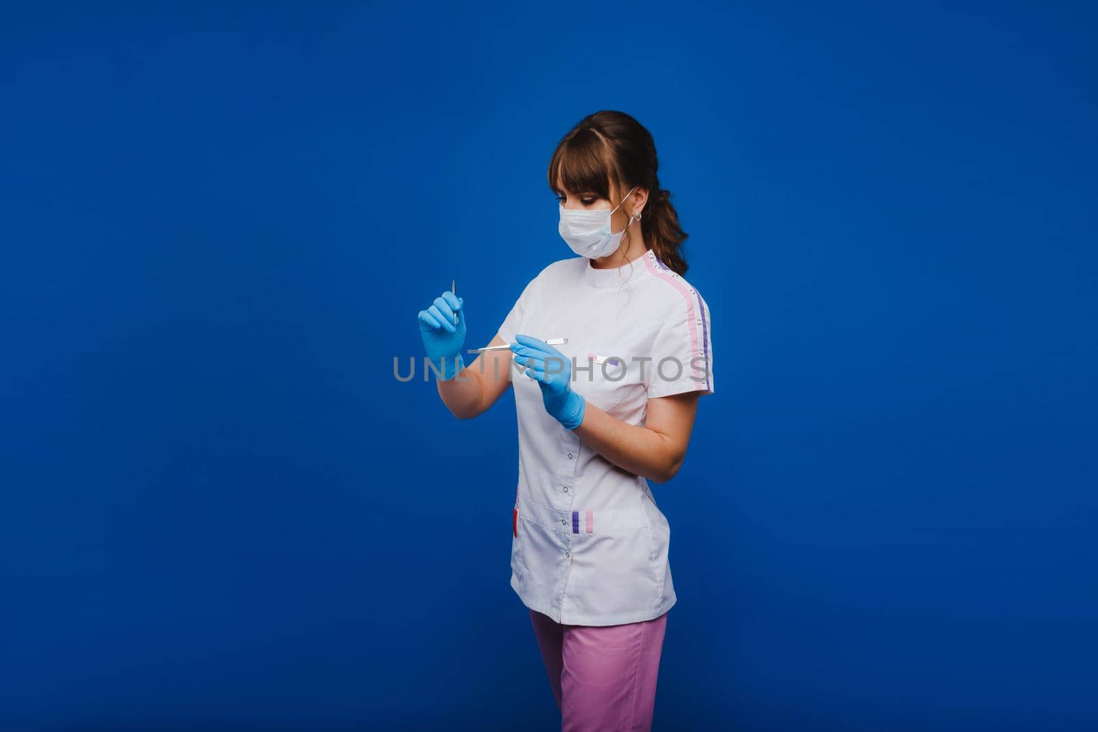 An attractive young female doctor holds a scalpel and looks directly at the camera. Concept of healthcare, treatment and surgery. Portrait of a medical practitioner on a blue background.