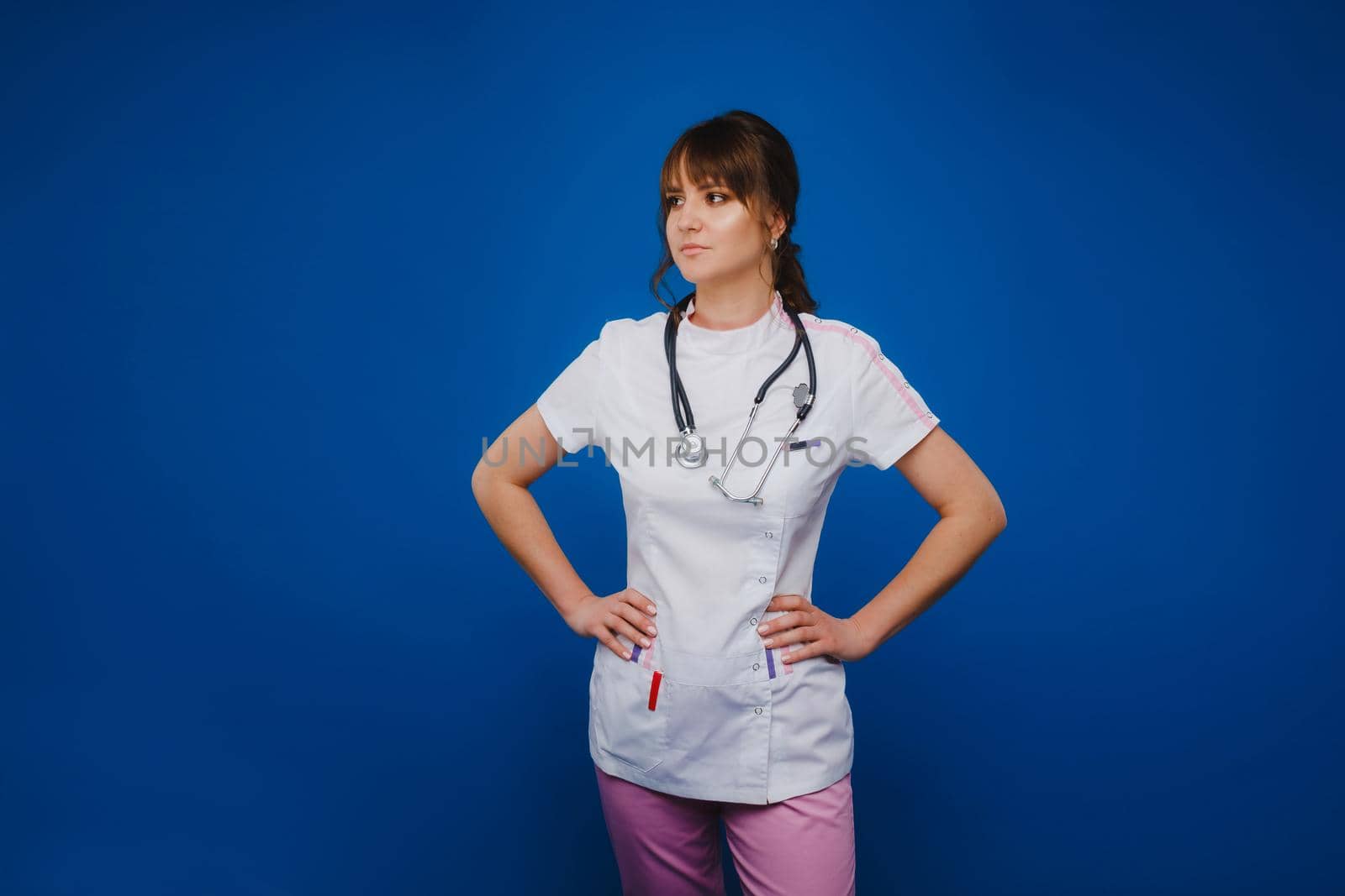 A female doctor, gesticulating, checks the heartbeat in the doctor's office at the hospital with a stethoscope isolated on a blue background by Lobachad