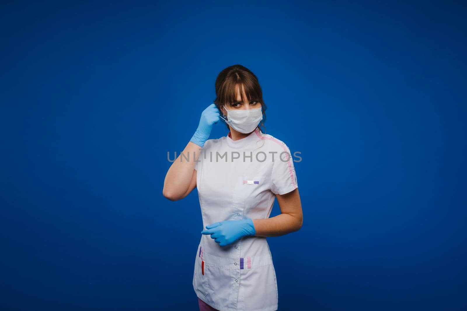 A doctor girl stands in a medical mask on an isolated blue background by Lobachad