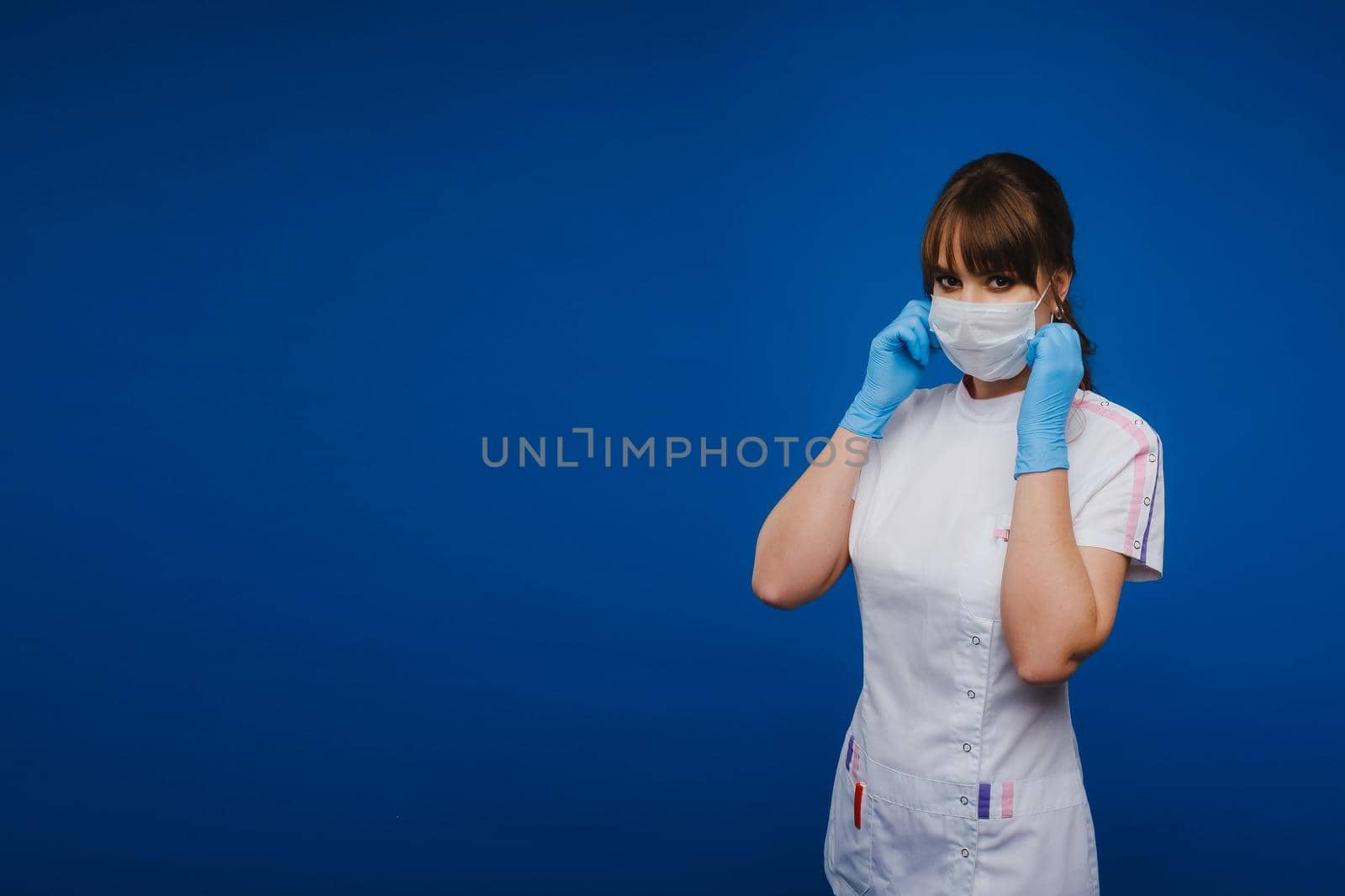 A doctor girl stands in a medical mask on an isolated blue background