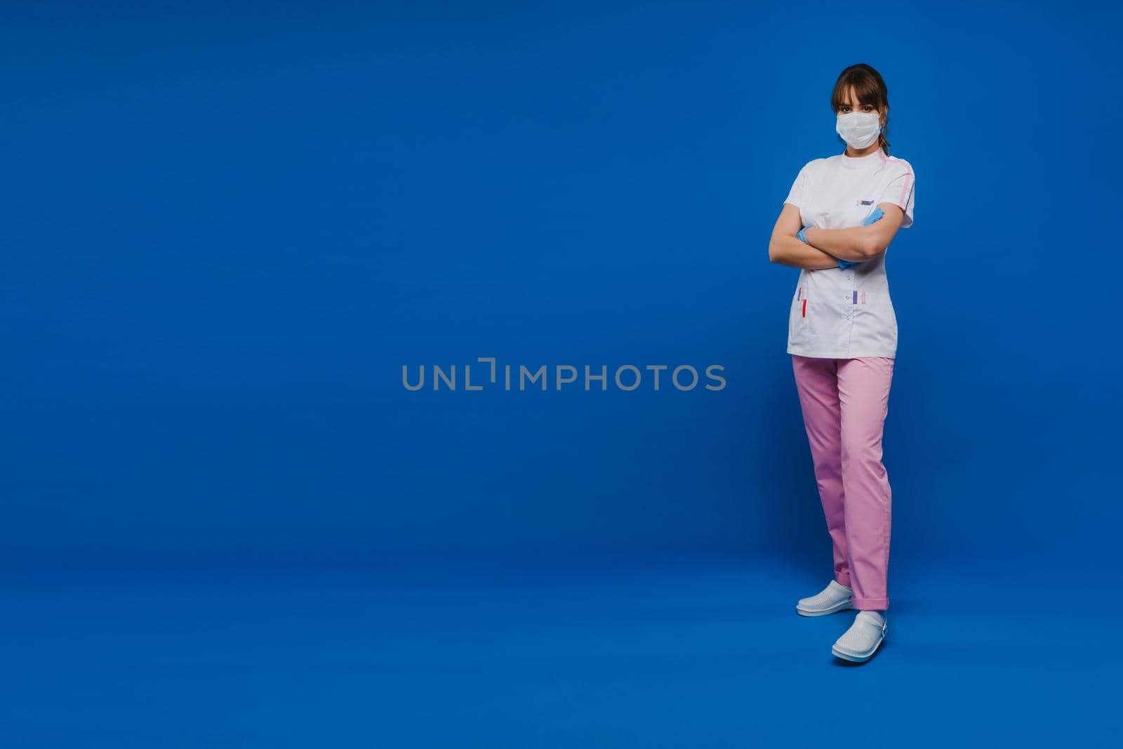 A girl doctor stands in a medical mask and gloves on an isolated blue background.