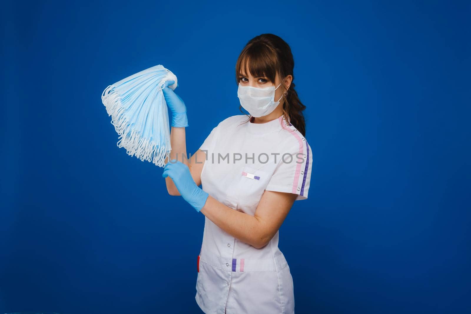 A young girl doctor in a medical mask holds a lot of masks in her hands. A nurse poses on a blue background.