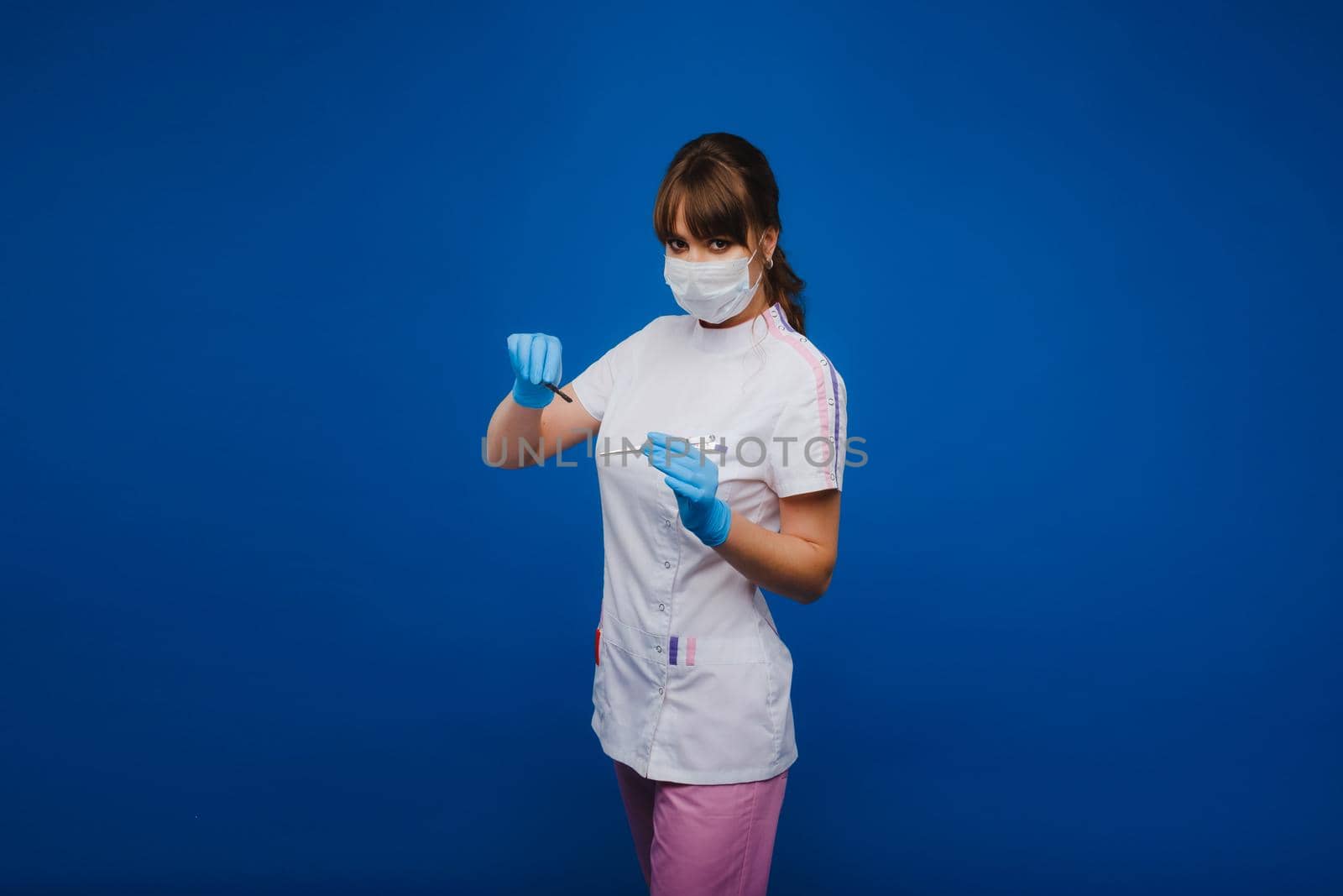 An attractive young female doctor holds a scalpel and looks directly at the camera. Concept of healthcare, treatment and surgery. Portrait of a medical practitioner on a blue background by Lobachad