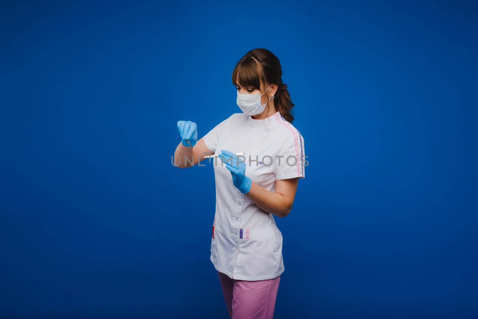 An attractive young female doctor holds a scalpel and looks directly at the camera. Concept of healthcare, treatment and surgery. Portrait of a medical practitioner on a blue background by Lobachad