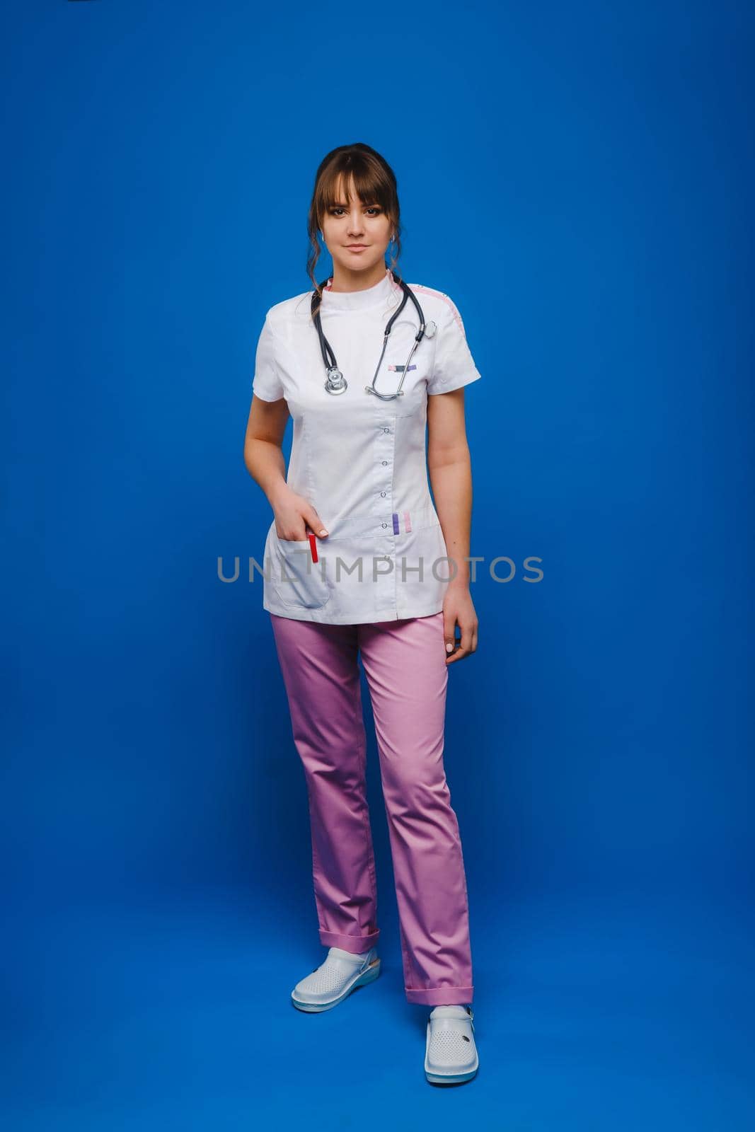 A female doctor, gesticulating, checks the heartbeat in the doctor's office at the hospital with a stethoscope isolated on a blue background.