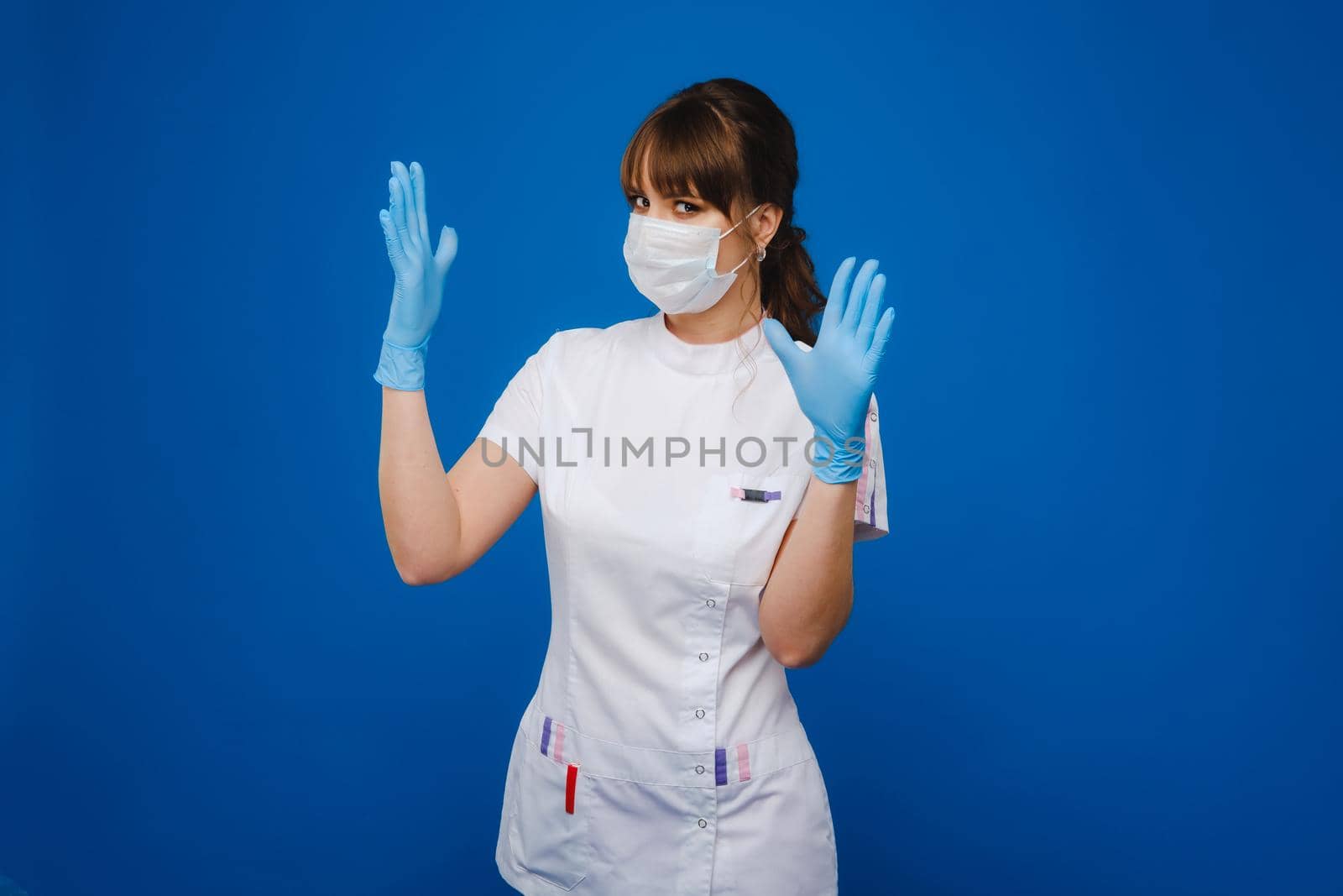 A girl doctor stands in a medical mask and gloves on an isolated blue background.