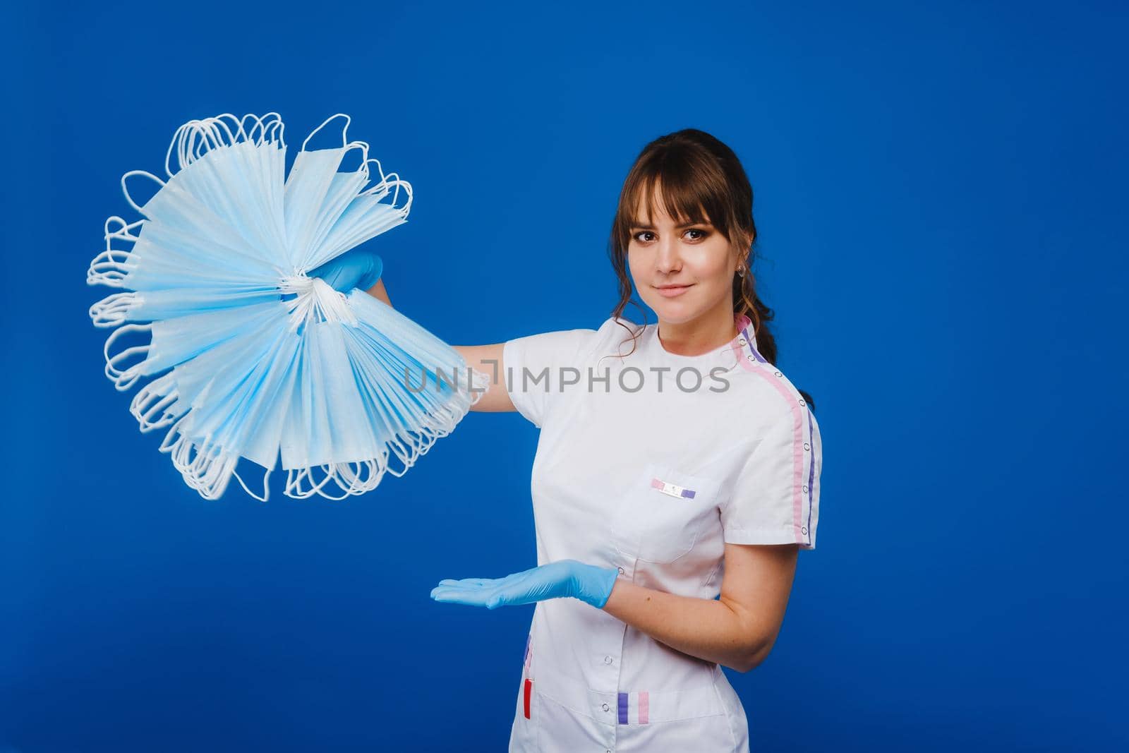 the doctor is holding a bunch of medical masks stacked together on a blue isolated background by Lobachad