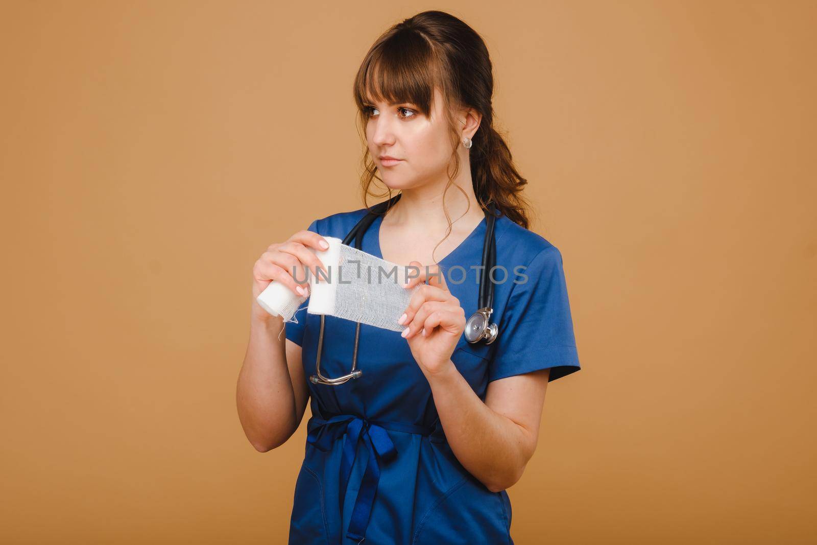 a female doctor in a white coat holds twisted gauze bandages for dressing wounds on a brown background by Lobachad