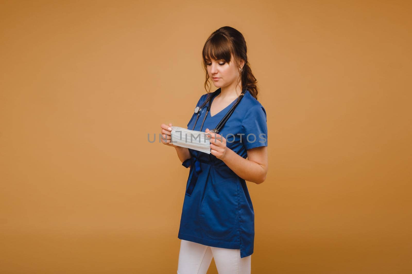A girl doctor stands in a medical mask, isolated on a brown background by Lobachad