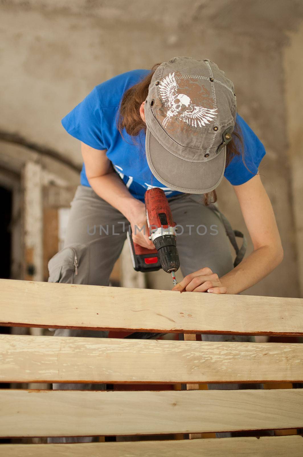 Ukraine, Goshcha, voluntary event, - August, 2021 - skilled young female worker is using power screwdriver drilling during construction wooden bench, gender equality, feminism. by balinska_lv