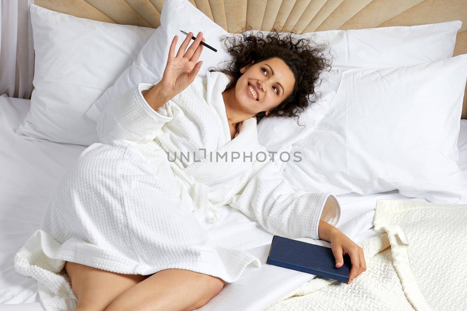 Woman wearing bathrobe Lying in Bed With Pen And Notepad