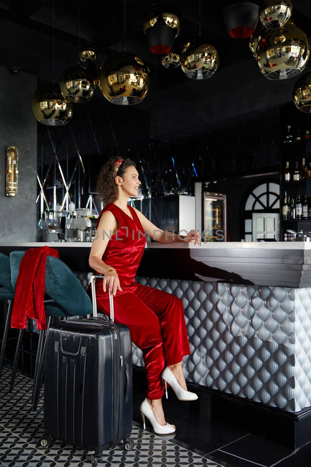 Young curly business woman in a lobby bar of hotel with suitcase. Travel concept