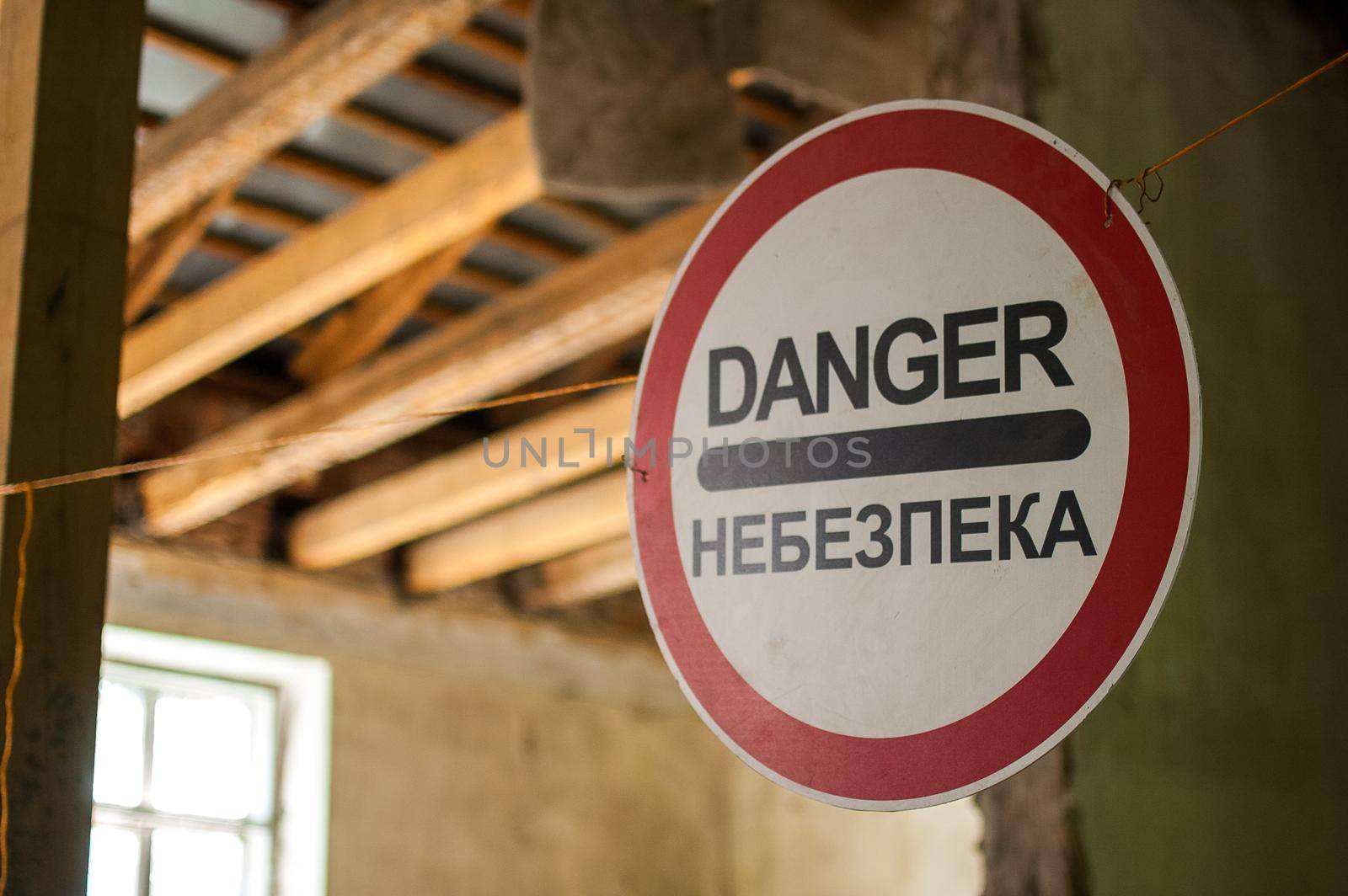 Old wrecked house with 'Danger' in English and in Ukrainian warning sign, abandoned building, uninhabitable place.