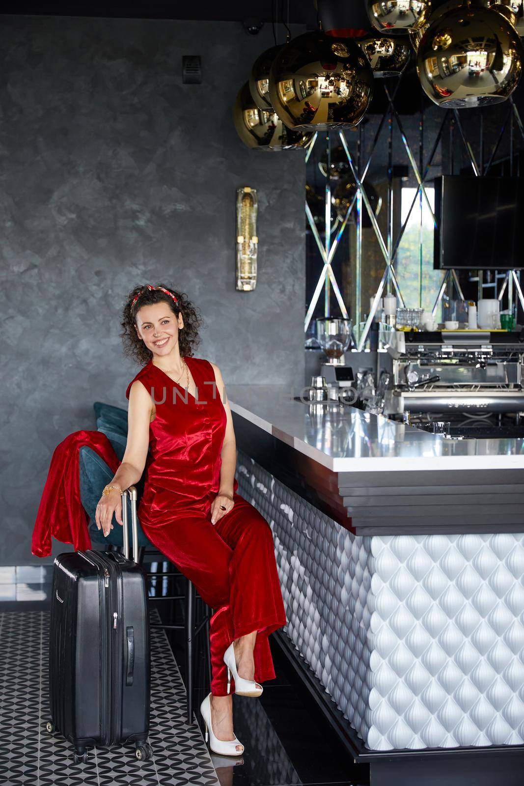 Young curly business woman in a lobby bar of hotel with suitcase. Travel concept