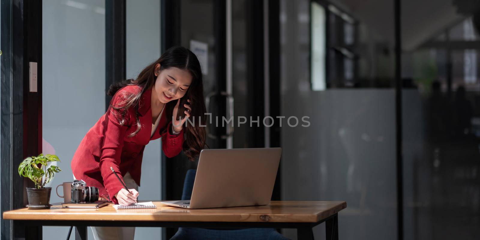 Woman entrepreneur managing her business from office working on laptop computer and discussing business using smartphone