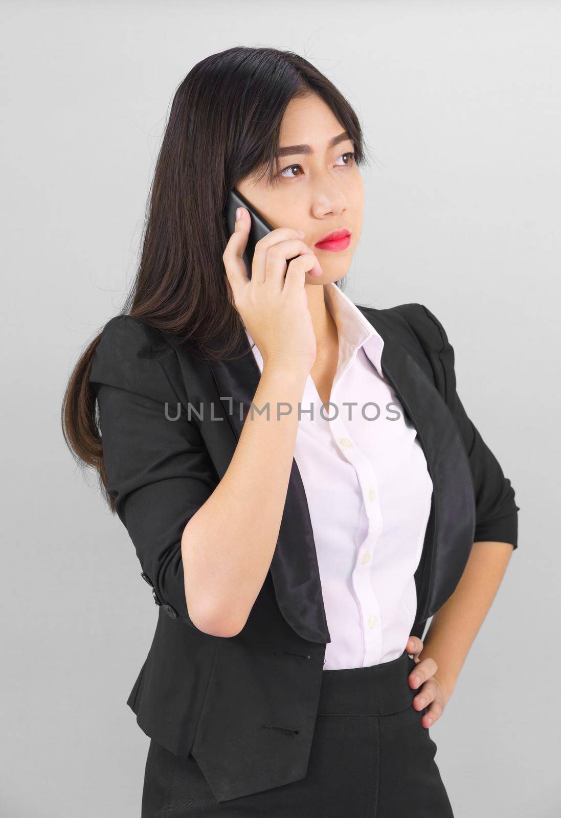 Young Asian women in suit standing posing using her phone against gray background