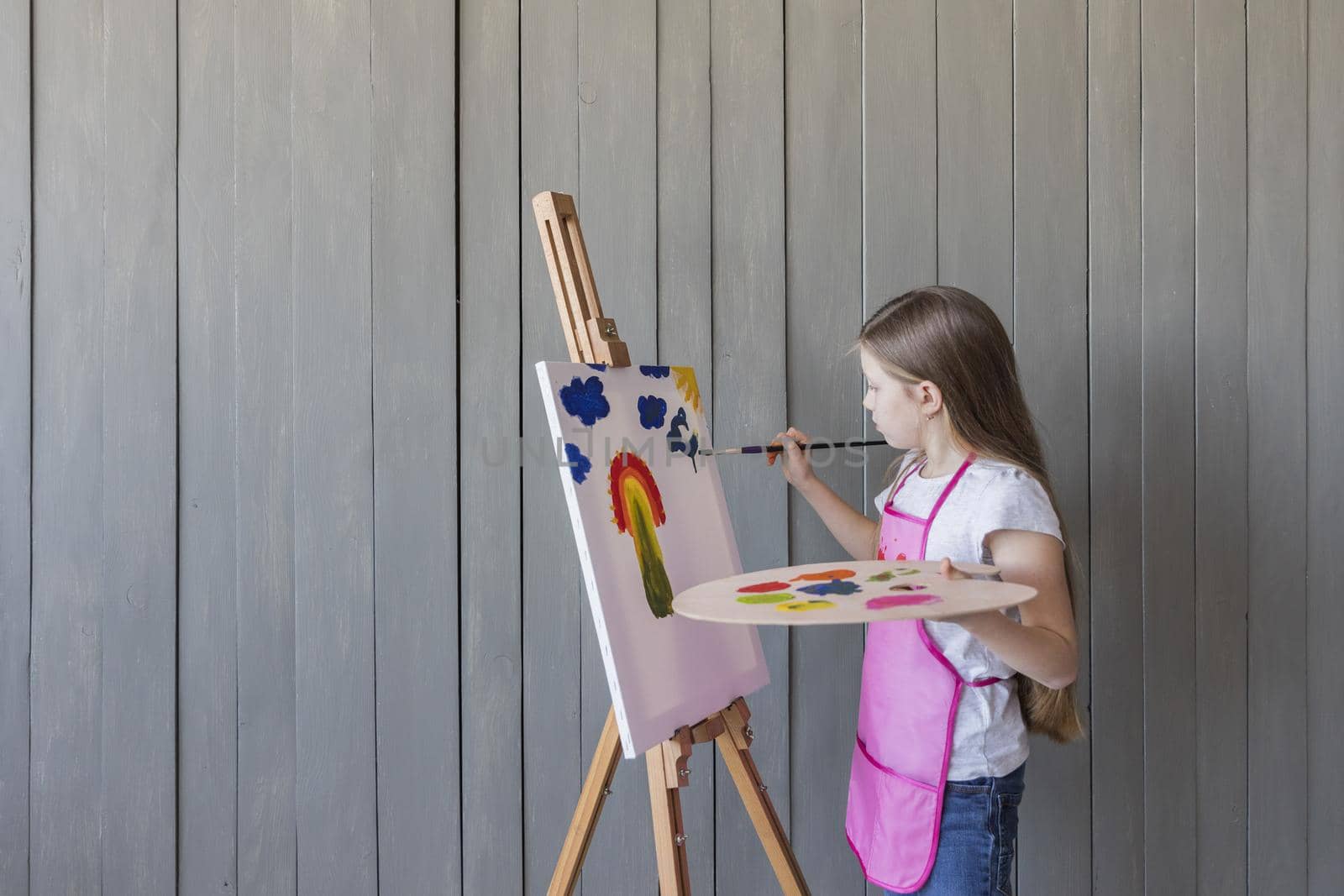 close up blonde girl painting with paint brush easel standing against gray wooden wall. Resolution and high quality beautiful photo