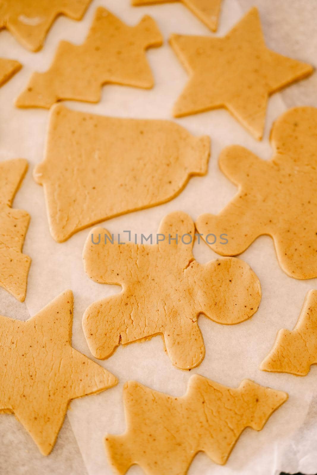 Process of making homemade cookies or gingerbread in different forms. Raw dough cookies lie on a baking sheet covered with parchment for baking before being sent to the oven. Close up by Nadtochiy