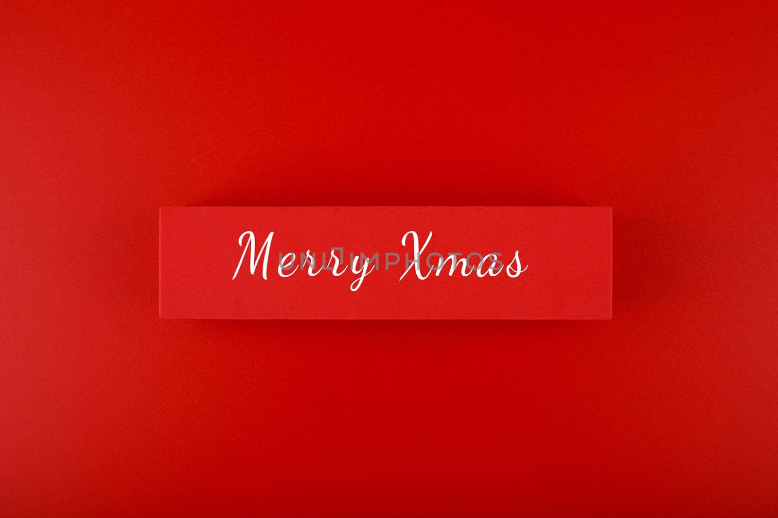 Minimal elegant flat lay Christmas theme. Merry Christmas text hand written on red tablet on red background. Creative layout in red colors