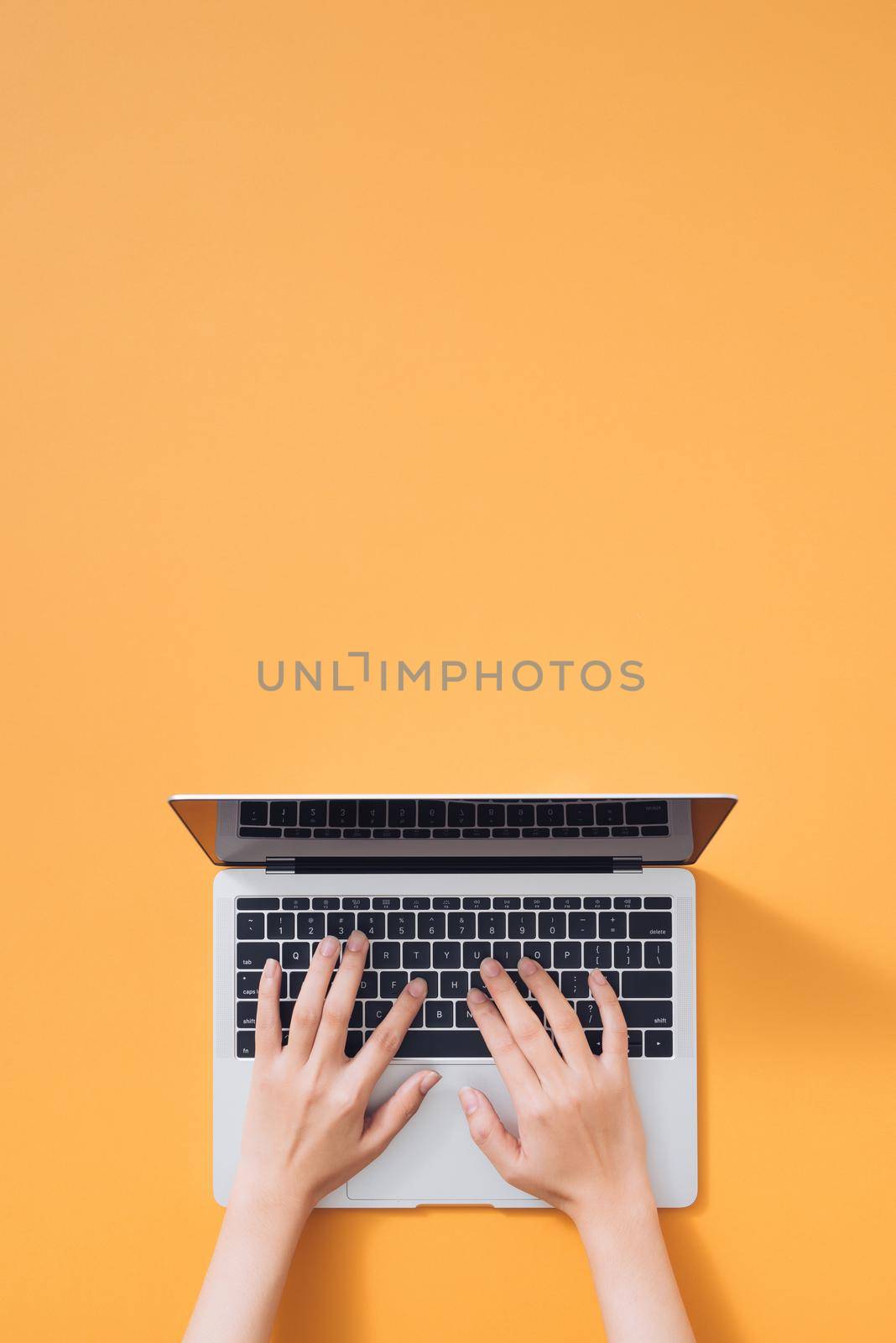 Flat lay of laptop, coffee and notebook on yellow background. Female hands typing on keyboard