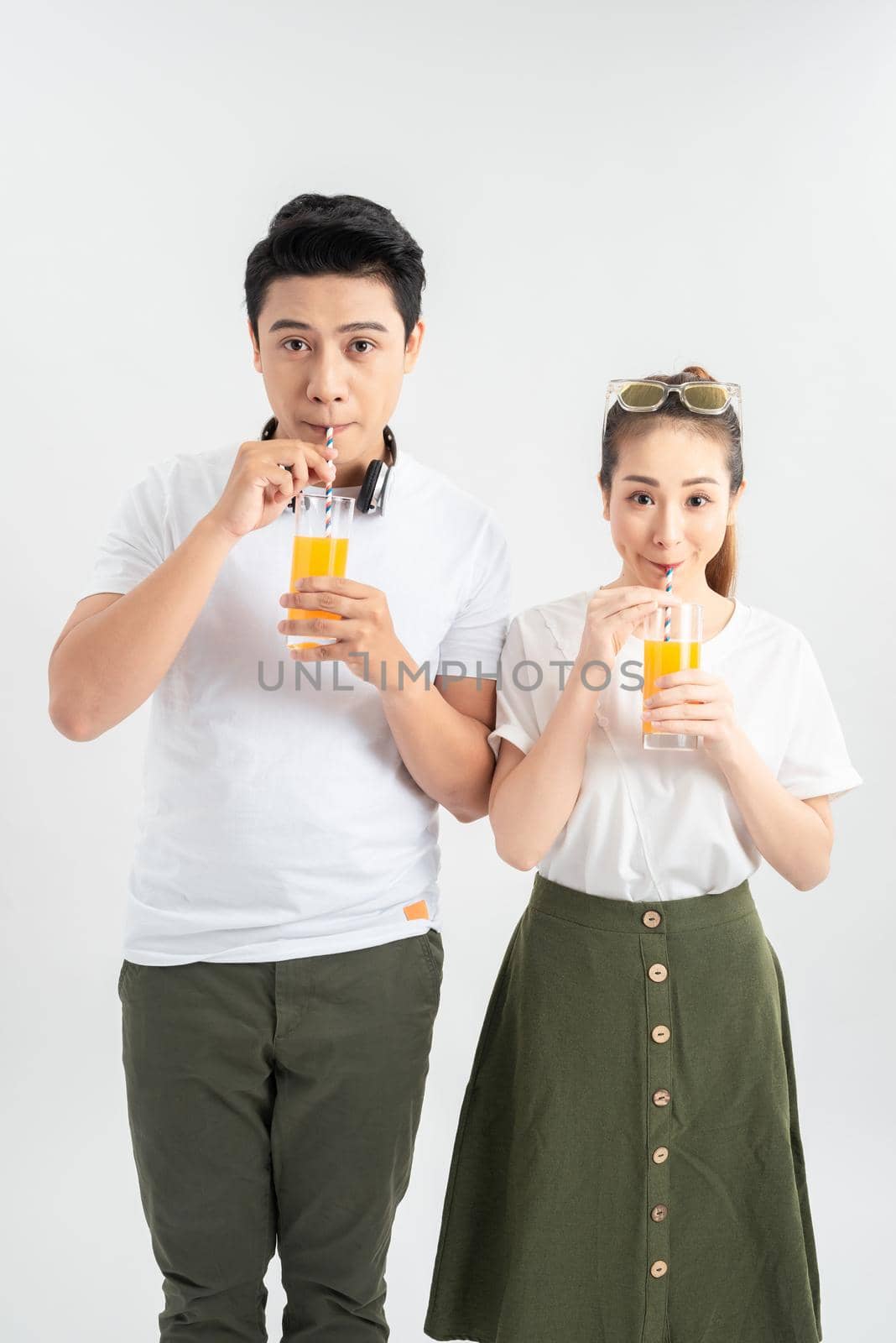 Stylish couple in casual clothes is drinking juice, looking at camera and smiling on white background by makidotvn