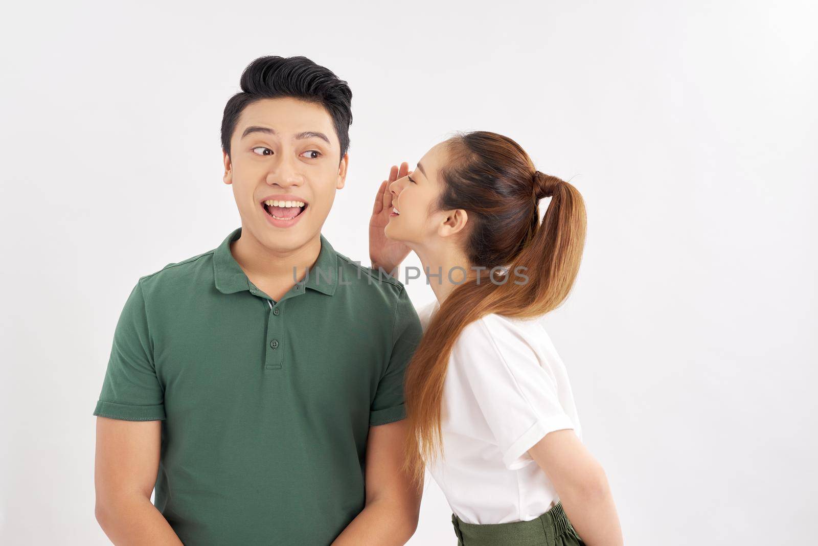 Excited asian couple standing isolated over white background, telling secrets to each other