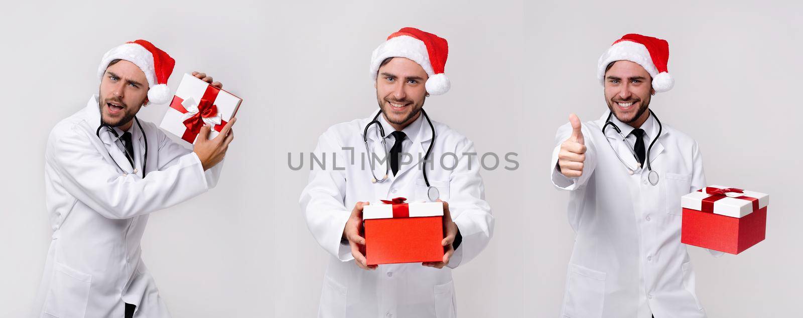 Young handsome doctor in white uniforme and Santa Claus hat standing in studio on white background smile and finger in camera by andreonegin