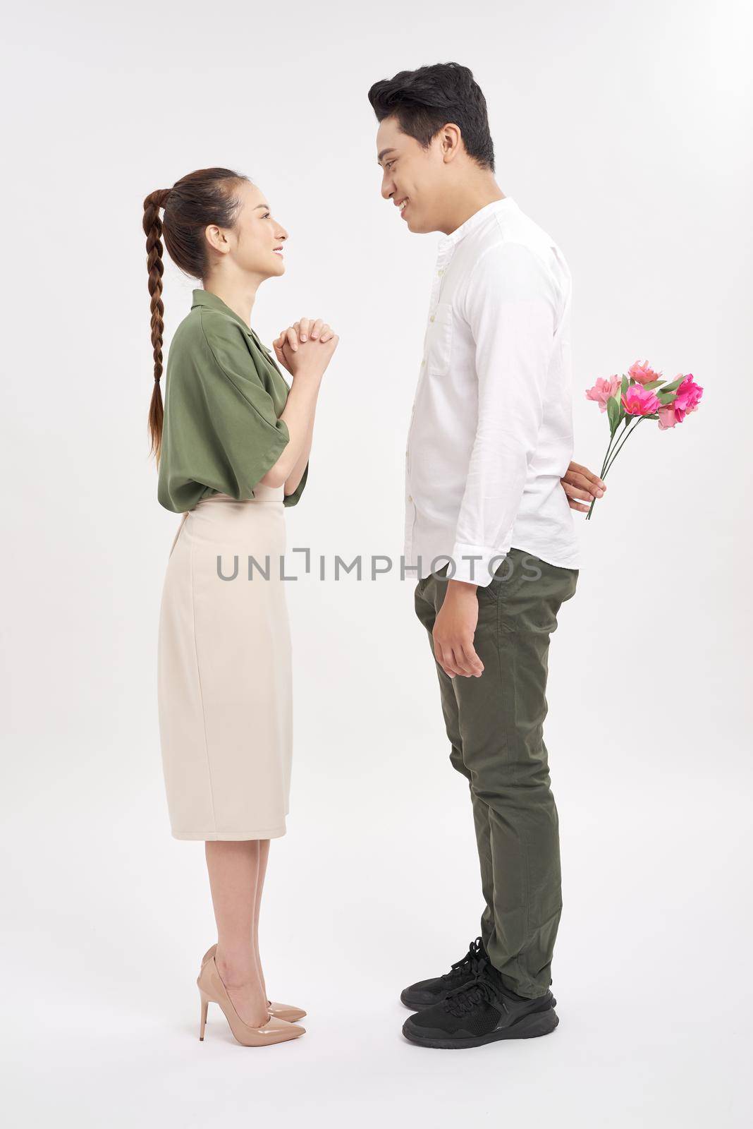 Young woman looking at man with flower bouquet behind the back.