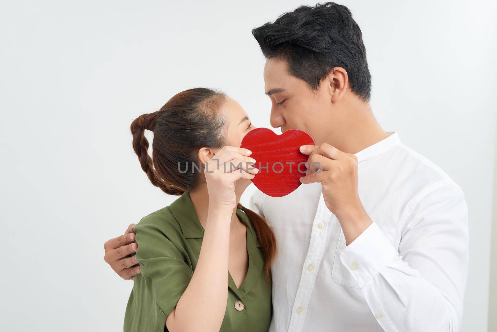 Attractive young couple kissing behind large heart on white background