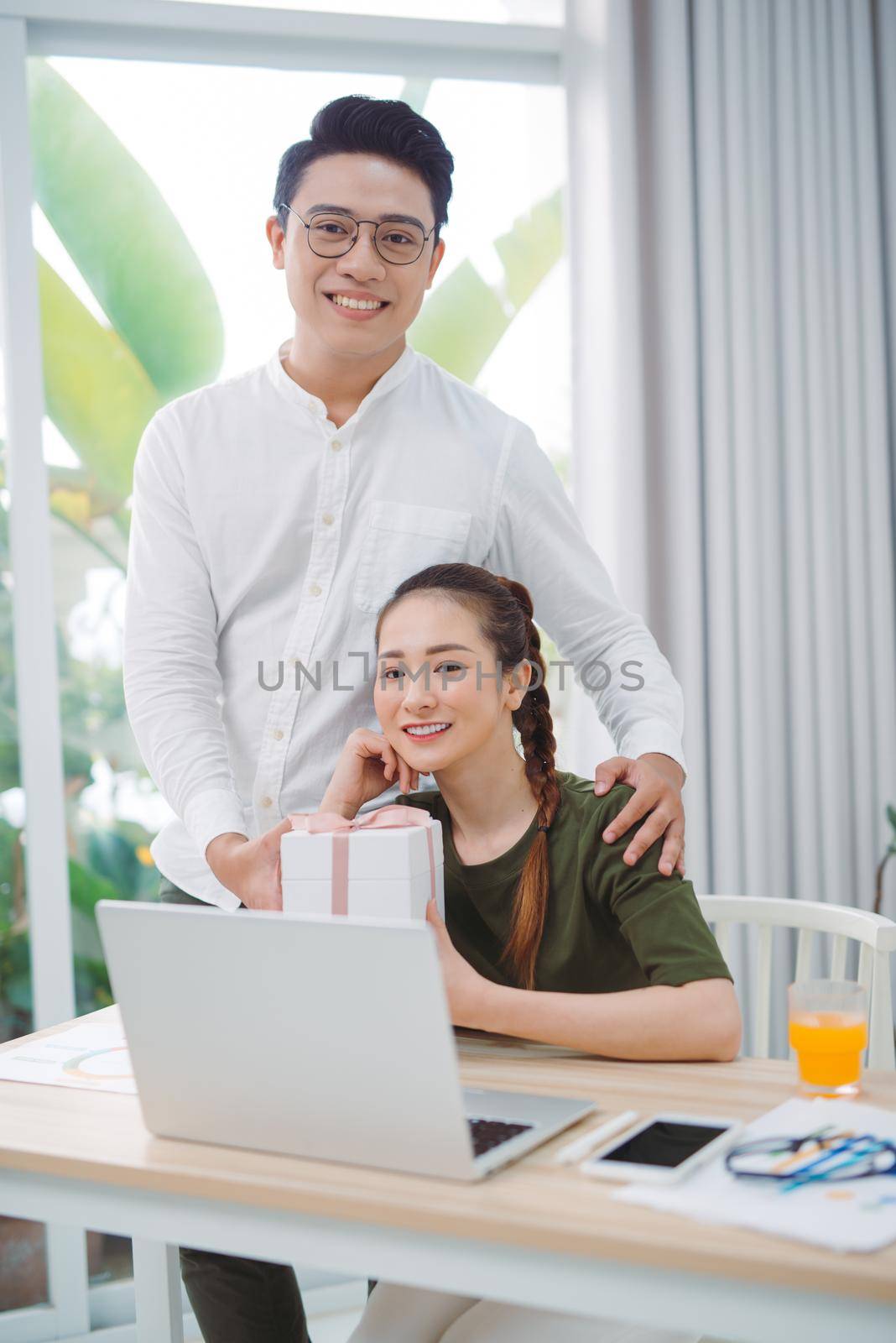 Young man in white shirt presenting gift to girl with laptop