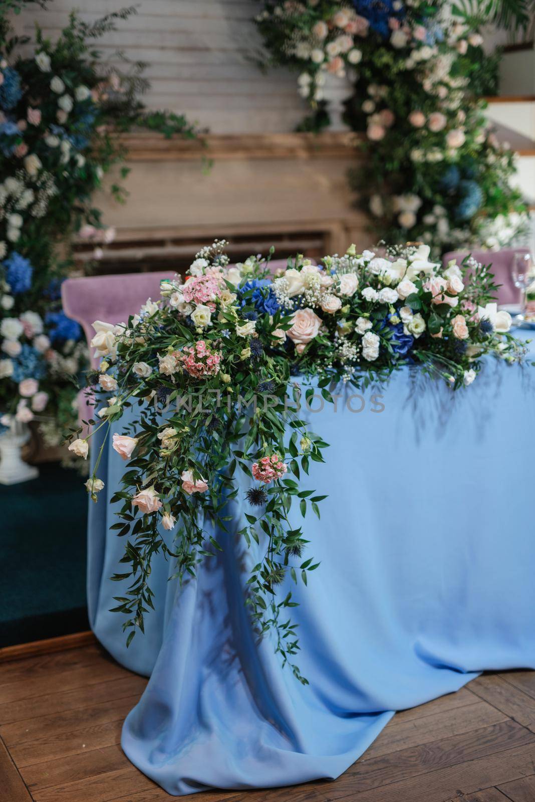 The presidium of the newlyweds in the banquet hall of the restaurant is decorated with candles and green plants, wisteria hangs from the ceiling